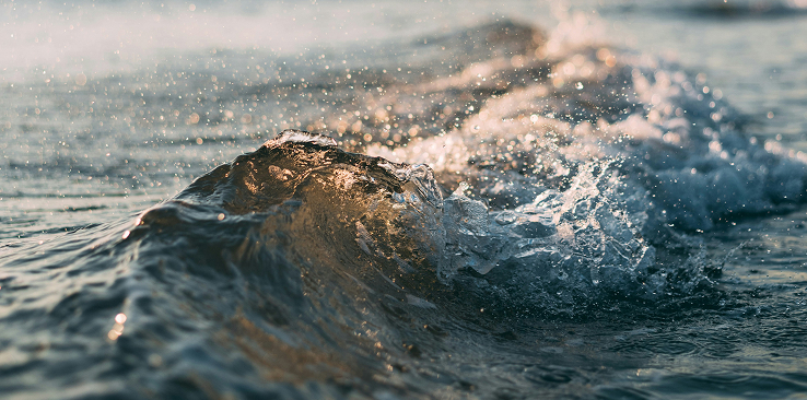 Close-up of a small ocean wave at sunset with golden reflections on the water.